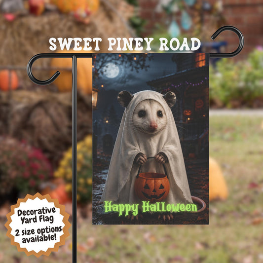 Halloween possum yard flag featuring a cute possum dressed in a white ghost costume holding a pumpkin candy bucket in a moonlit autumn yard with spooky Halloween decorations and glowing lights.