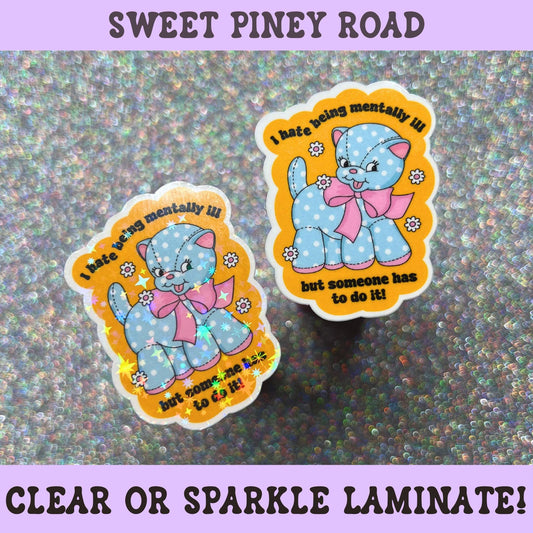Cute plush blue cat sticker with pink bow and flowers featuring the phrase "I Hate Being Mentally Ill But Someone Has To Do It," combining mental health humor, anxiety humor, and kawaii aesthetics.