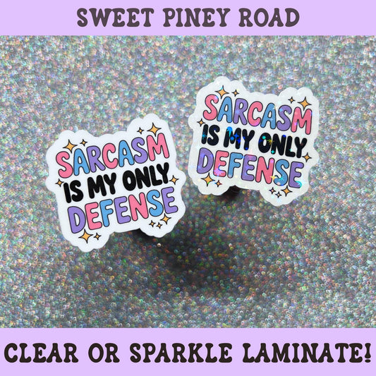 Colorful sticker featuring the phrase "Sarcasm Is My Only Defense" in pink, blue, purple, and black lettering with decorative stars.